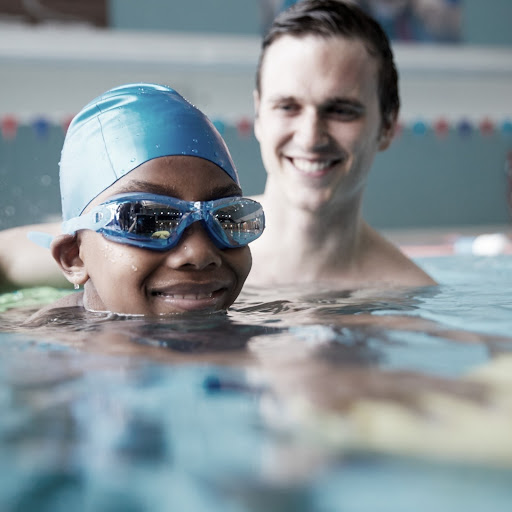 child with goggles with instructor smiling in pool