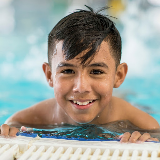 boy holding onto side of pool smiling