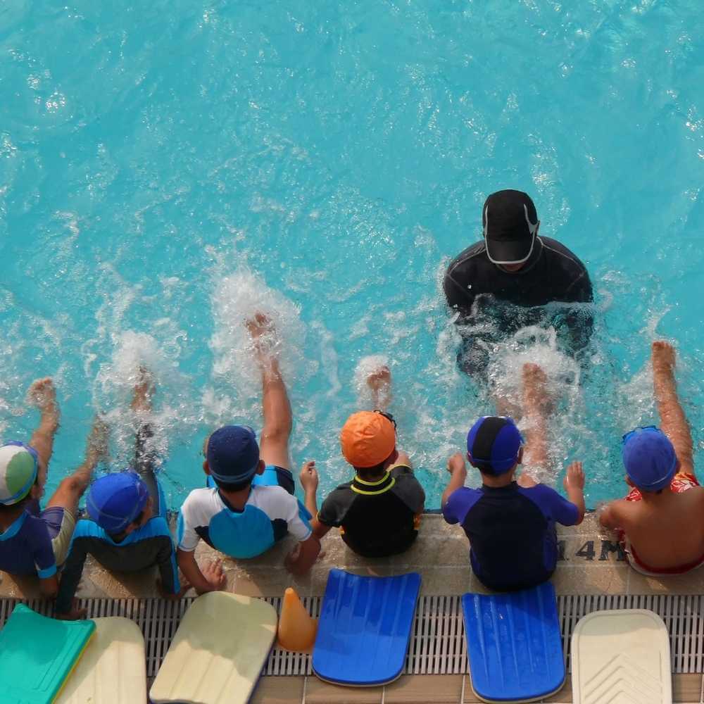 swimming coach with a group of younger swimmers with kickboards behind them